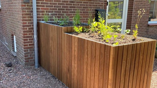 Warmtepomp geïntegreerd in houten plantenbak naast gevel van woning