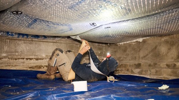 Monteur die REF Insulation isolatiefolie aanbrengt in een kruipruimte tijdens een renovatieproject.