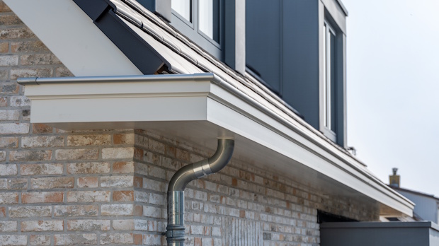 Gutter and curved downspout on a brick house under a sloped roof, directing rainwater away from the wall.