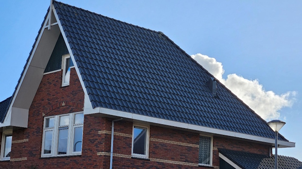 Brick house with a steep blue tile roof, white trim, and a clear blue sky above.